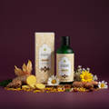 A bottle of Eccecosmetics Body Oil next to its matching patterned box, styled with ginger root, sliced yellow turmeric, daisies, and other flowers on a deep purple background.