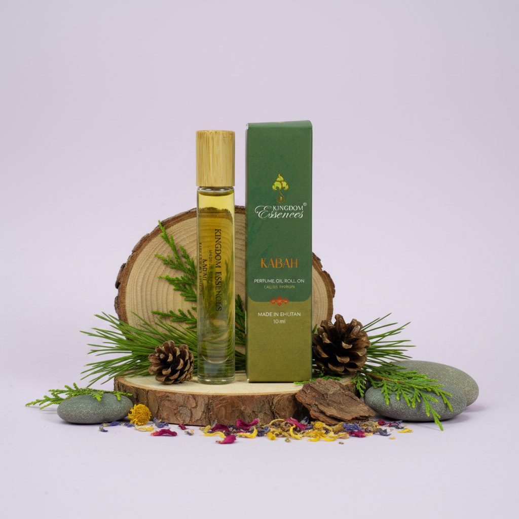 A bottle of Kabah Perfume Oil next to its green box, styled with pine branches, pinecones, and small stones on a light purple background.